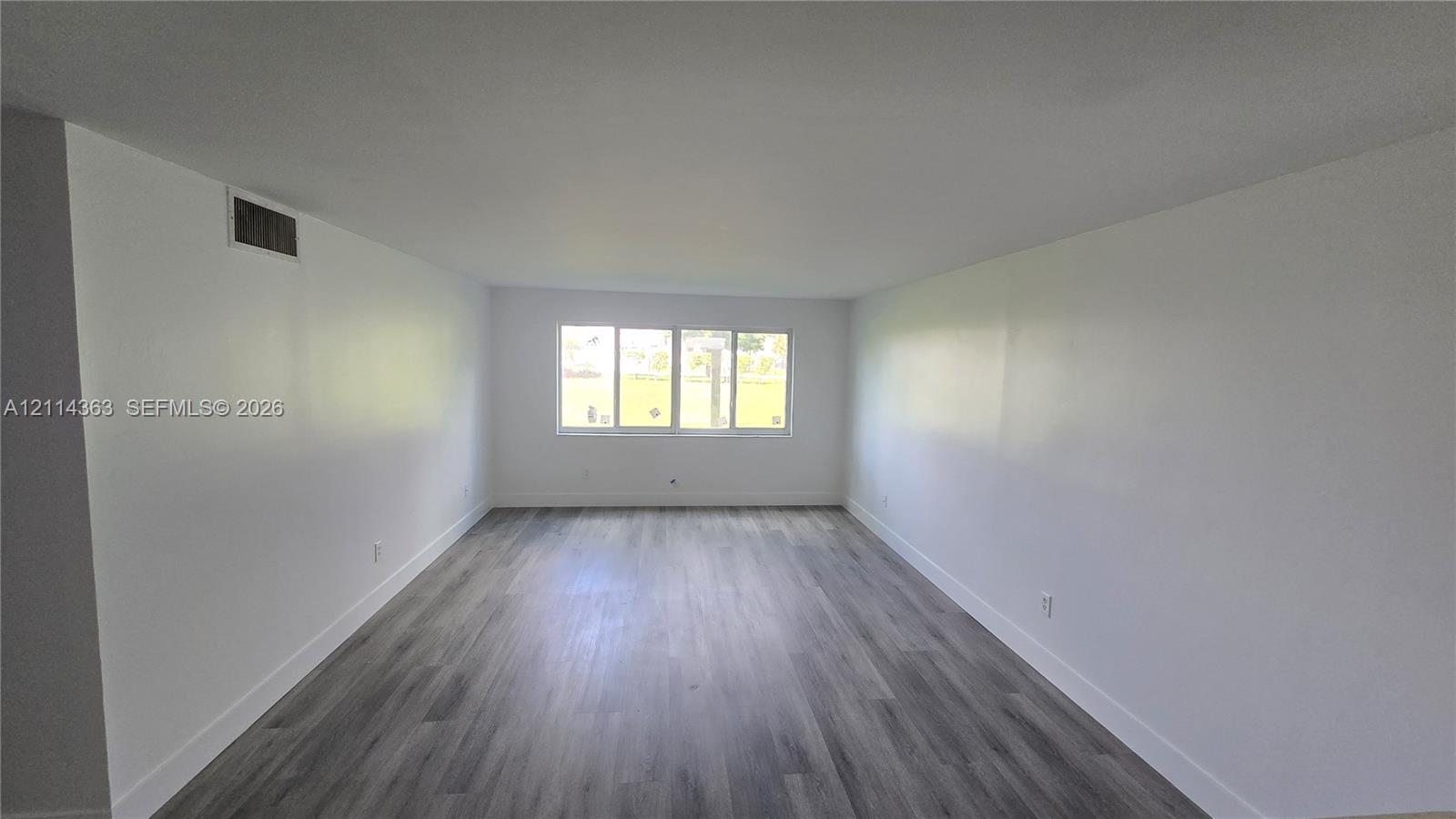 Open-concept interior space featuring wood-finish flooring and expansive white walls, illuminated by a multi-pane window