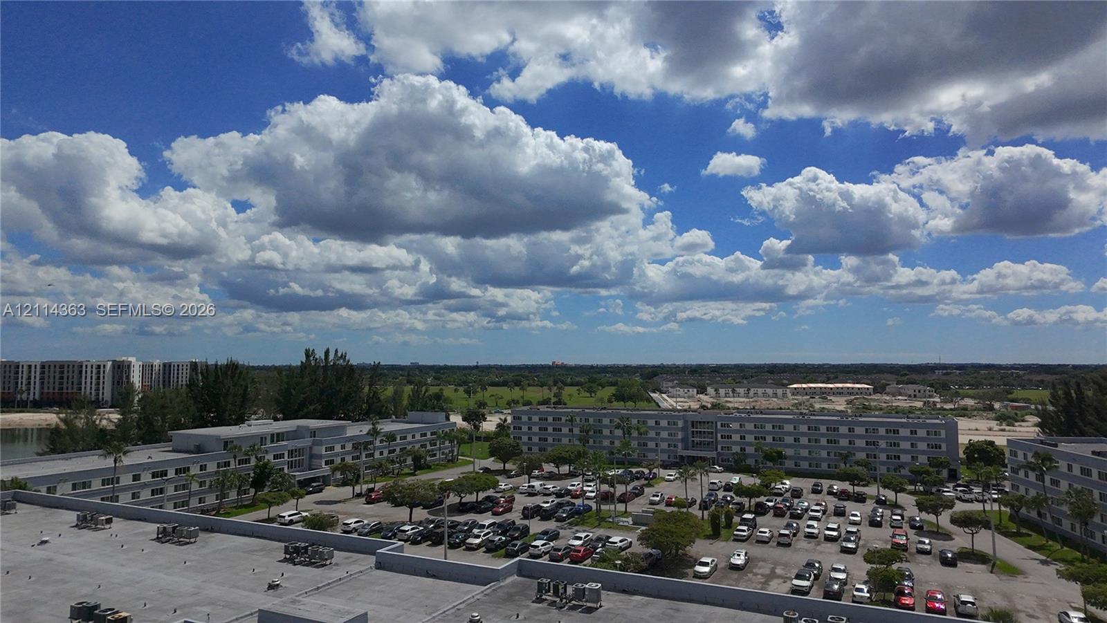 Aerial perspective featuring multi-story residential buildings, paved surface parking lots, and landscaped grounds with mature palm trees