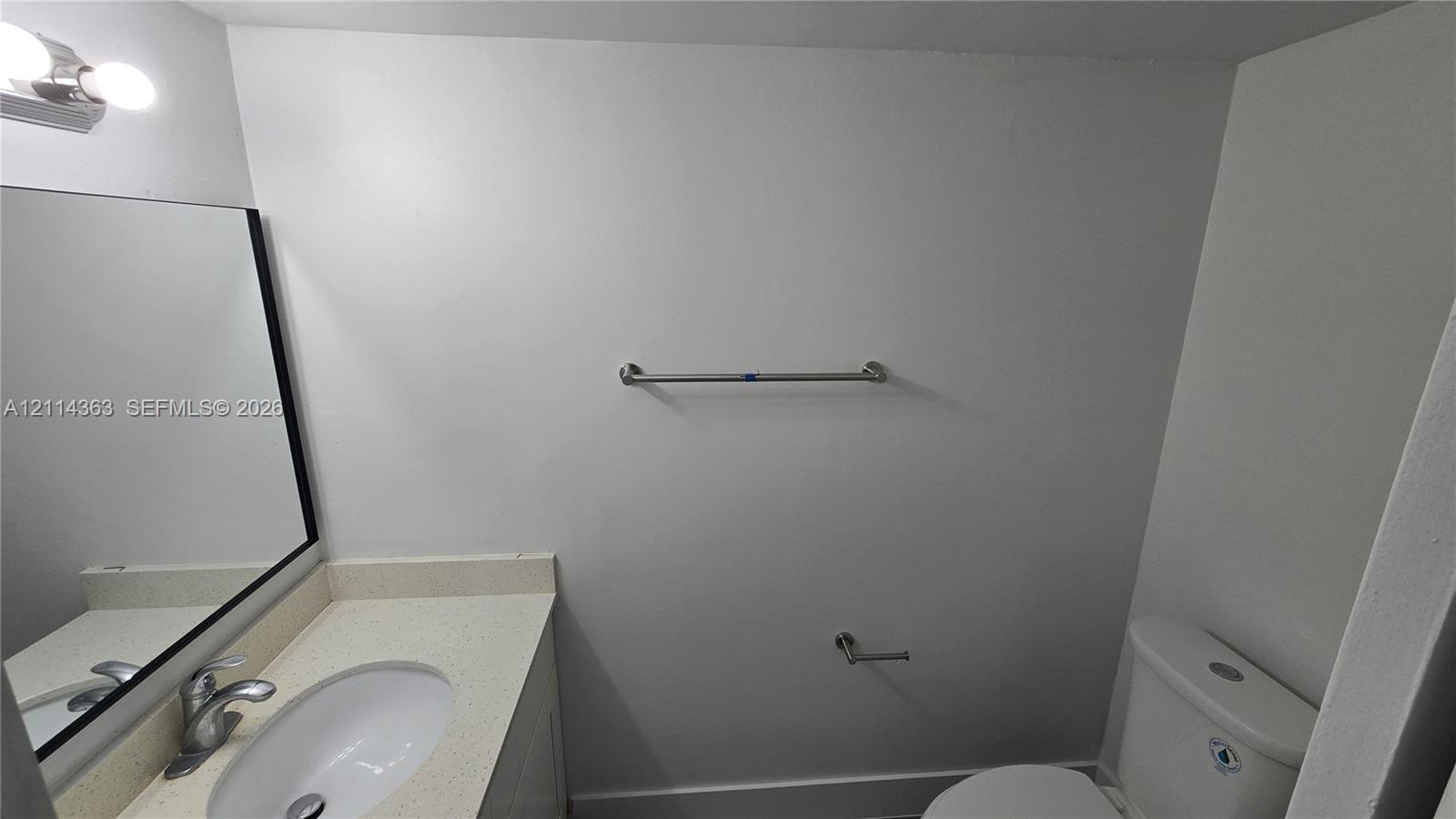 Vanity featuring a solid-surface countertop with an integrated oval basin, polished chrome faucet, rectangular mirror with a dark frame, and wall-mounted light fixture