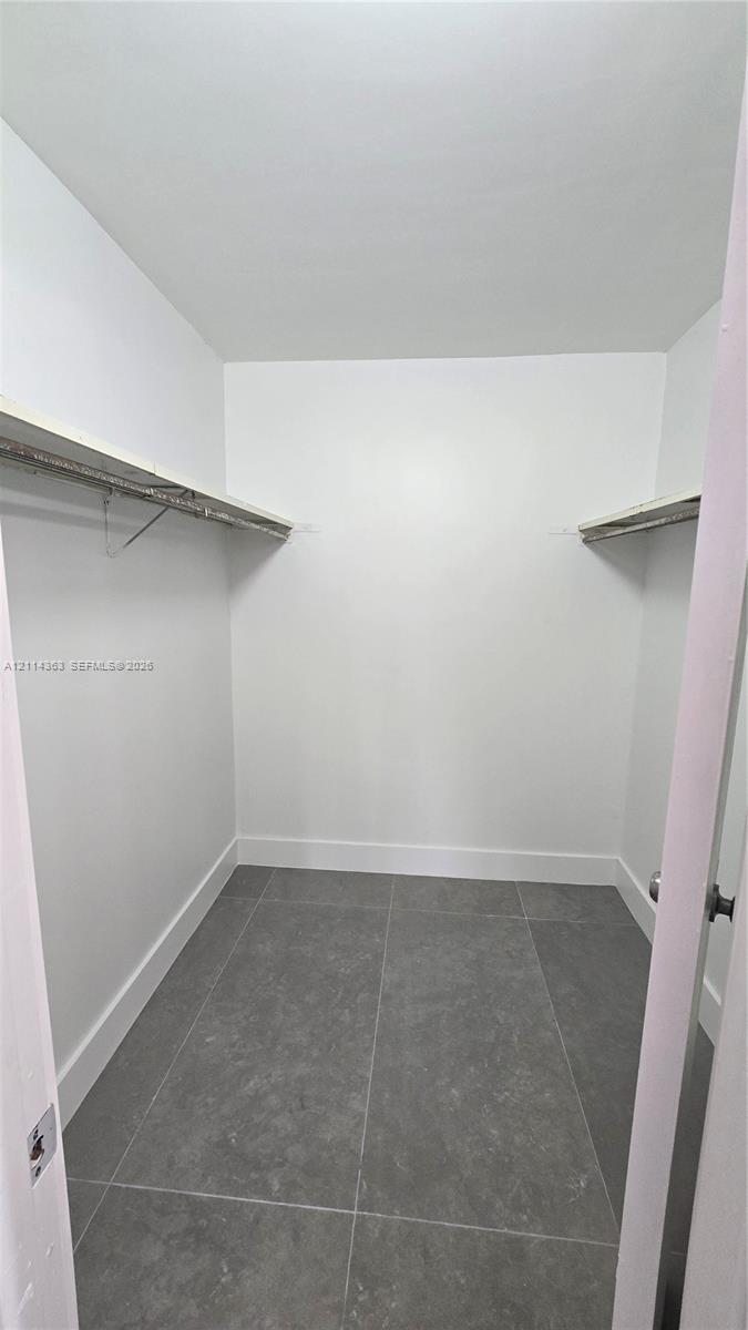 Walk-in closet featuring grey stone-finish tile flooring and dual overhead shelving with integrated clothing rods