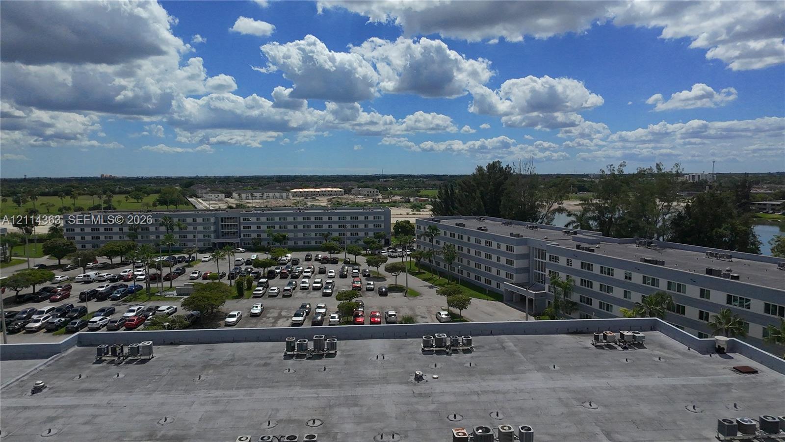 Aerial perspective of a multi-story residential building featuring a flat roof with exterior-mounted HVAC units and an expansive asphalt parking lot