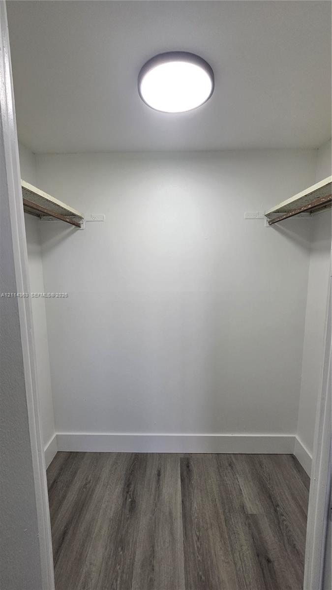 Storage space featuring wood-finish flooring, two fixed shelving units with integrated clothing rods, and a ceiling-mounted flush light fixture