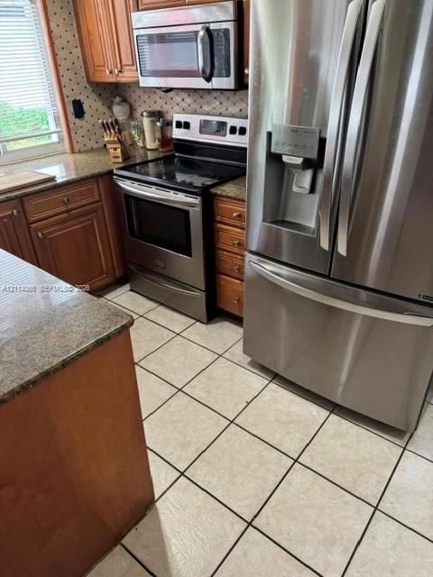 Kitchen featuring wood cabinetry, stone countertops, tiled flooring, and stainless steel appliances including a refrigerator, range, and over-the-range microwave
