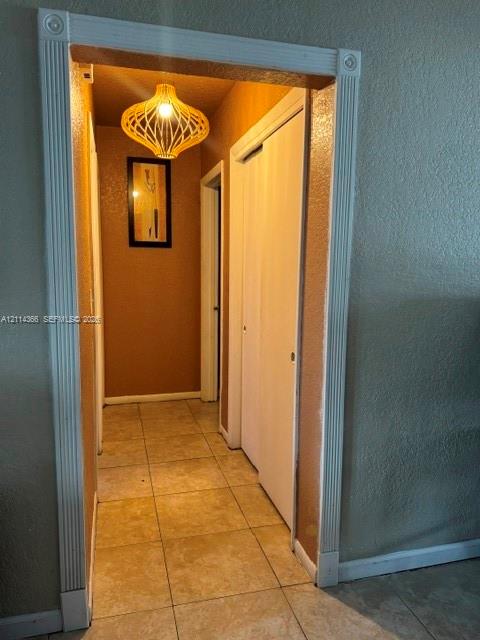 Hallway featuring fluted casing trim, tile flooring, built-in closet with bi-fold doors, and a pendant light fixture
