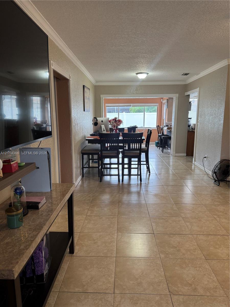 Neutral-toned tile flooring, crown molding, and large windowed openings providing natural light