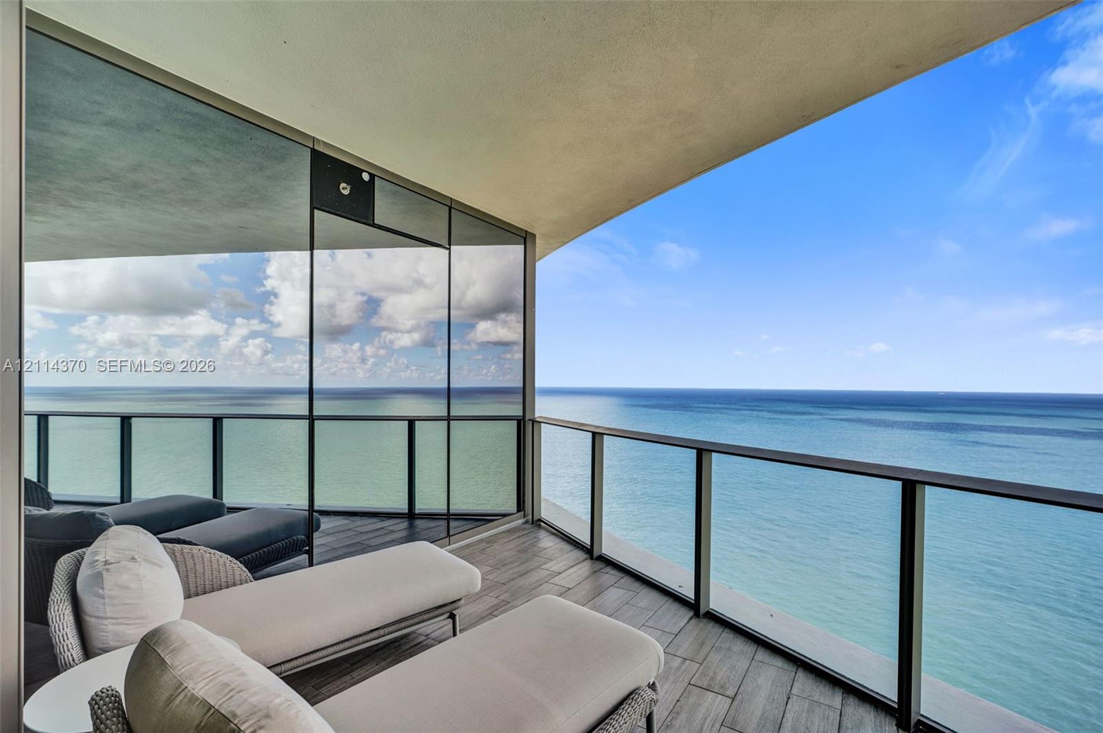 Covered private balcony featuring tile flooring, floor-to-ceiling glass paneling, and metal railing overlooking the ocean