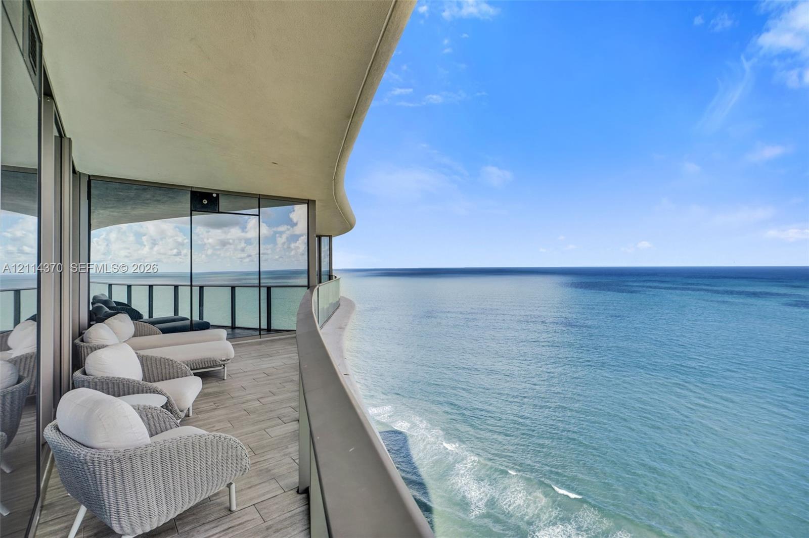 Curved balcony featuring wood-finish tile flooring, floor-to-ceiling glass paneling, and a glass balustrade overlooking the ocean
