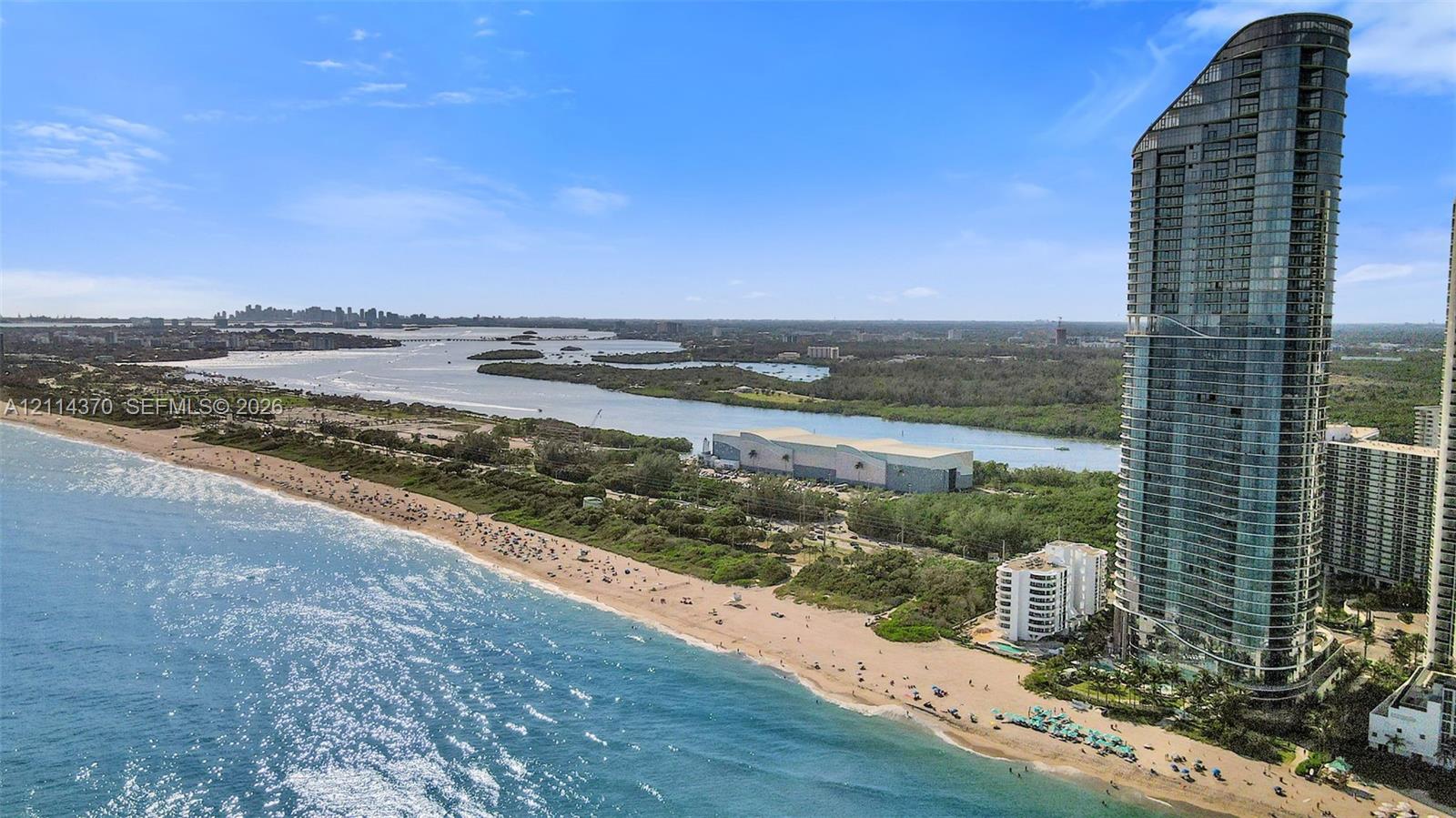 High-rise architectural exterior featuring a glass-paneled facade, positioned along a coastline with direct sandy beach frontage and proximity to tidal waterways