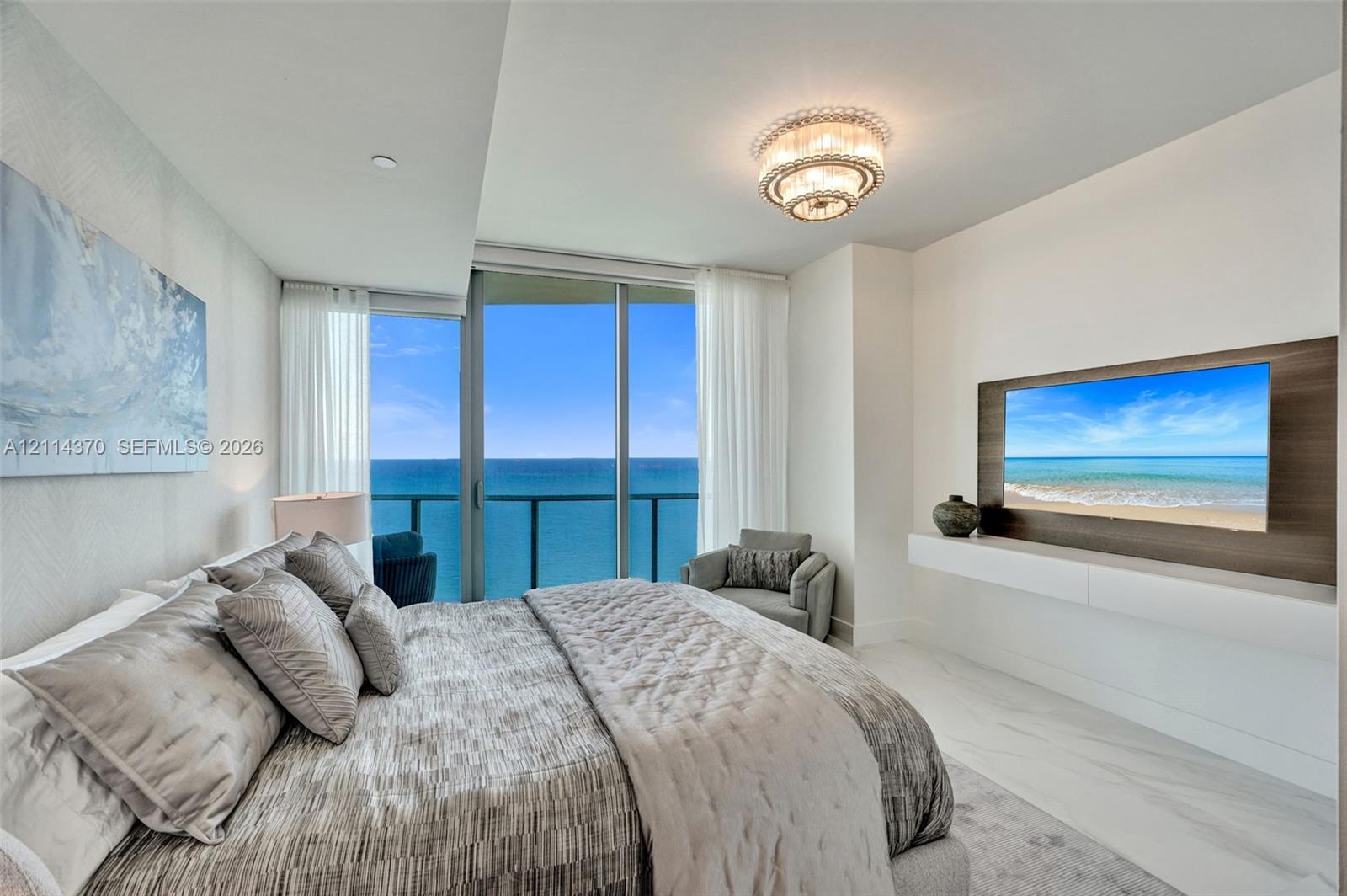 Floor-to-ceiling glass sliding doors, wood-finish media wall panel, wall-mounted floating console, stone-finish tile flooring, and tiered crystal flush-mount light fixture