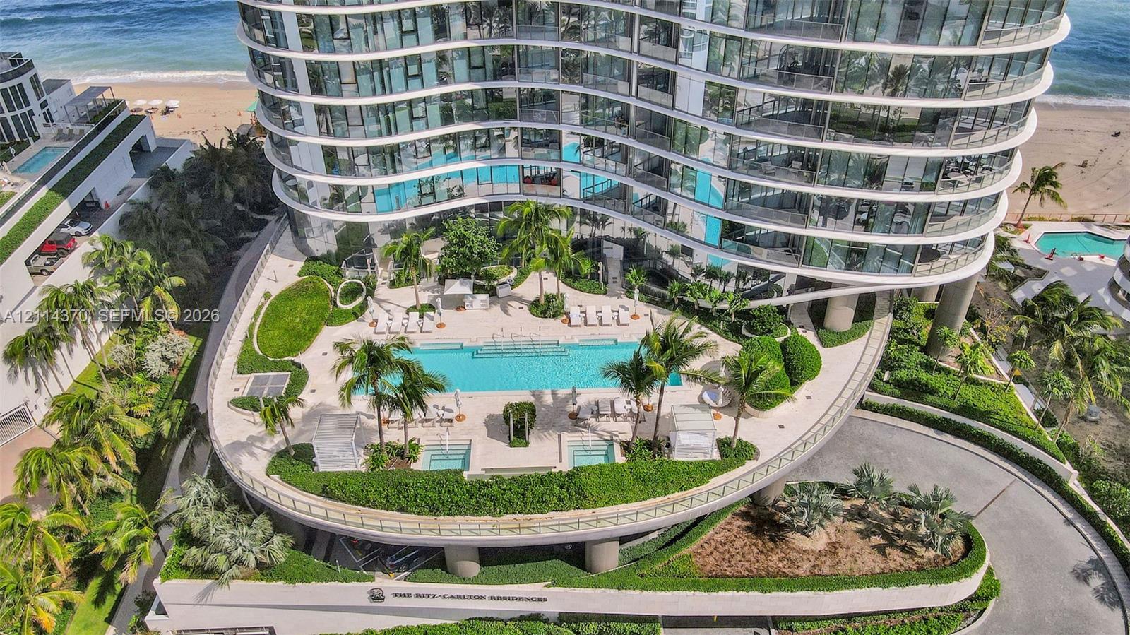 High-rise tower featuring a curved glass facade, an elevated pool deck with two integrated hot tubs, and meticulously maintained tropical landscaping
