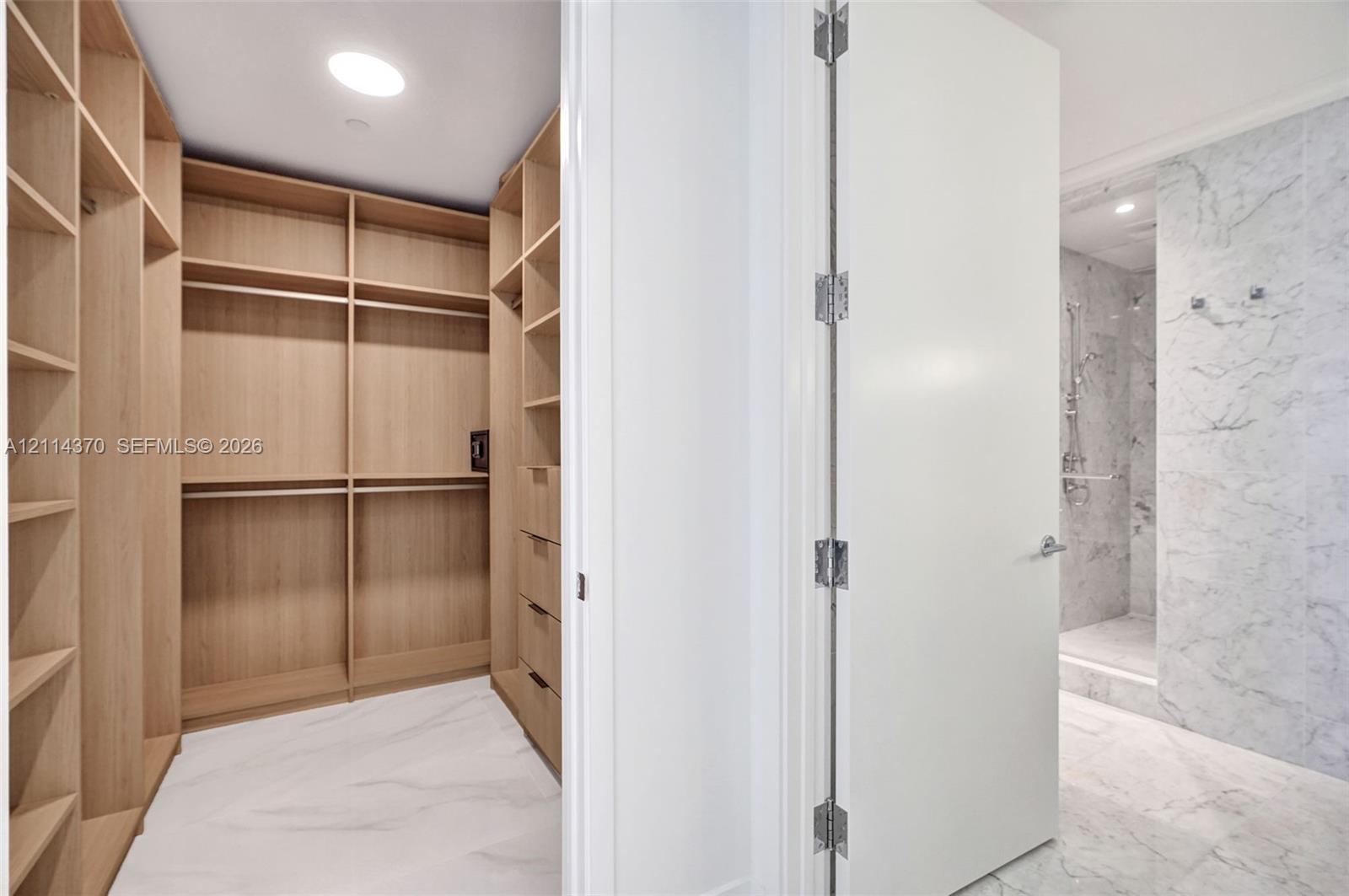 Custom wood-finish shelving and cabinetry, stone-pattern flooring, and a walk-in shower featuring floor-to-ceiling stone-pattern tile