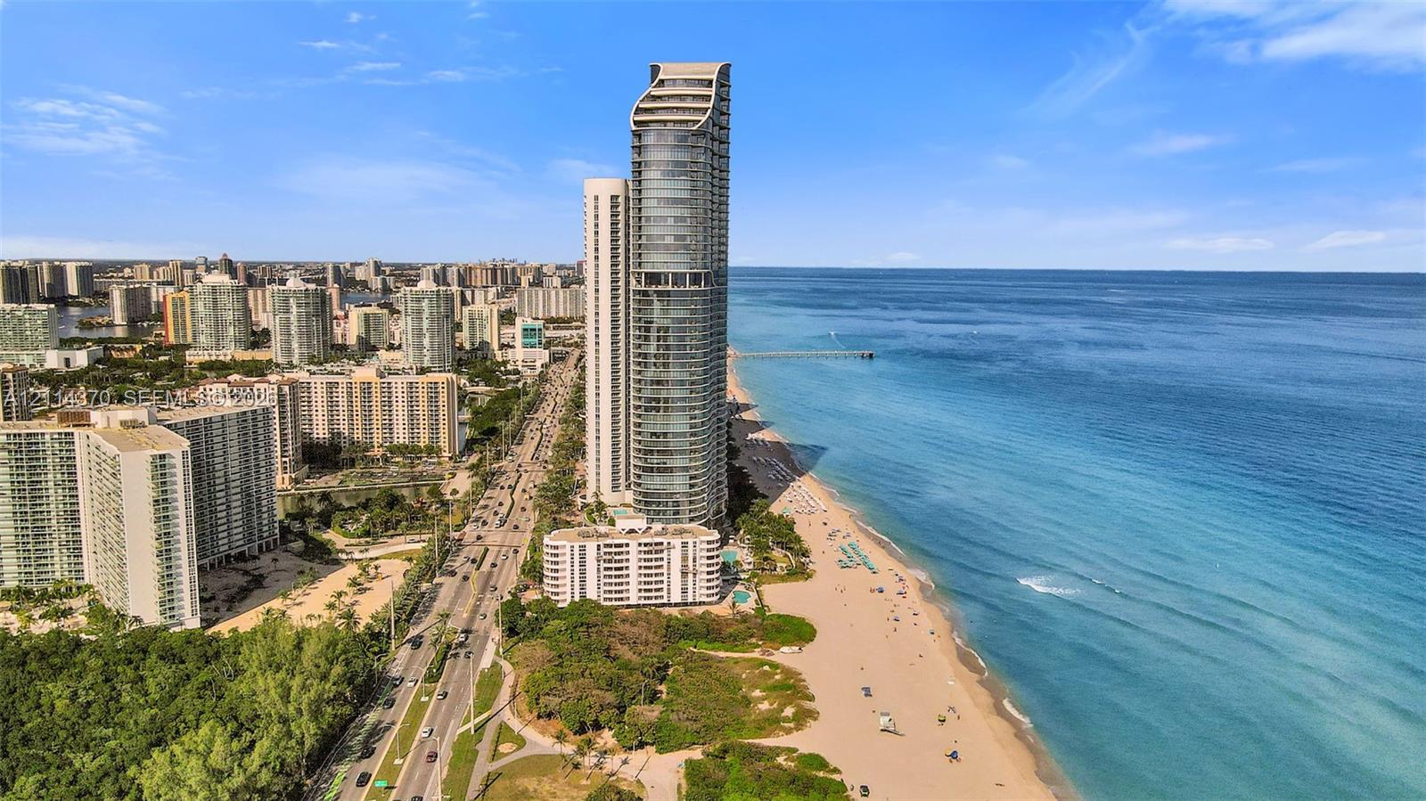 High-rise residential tower featuring a glass facade, oceanfront positioning, direct beach access, and coastal scenery
