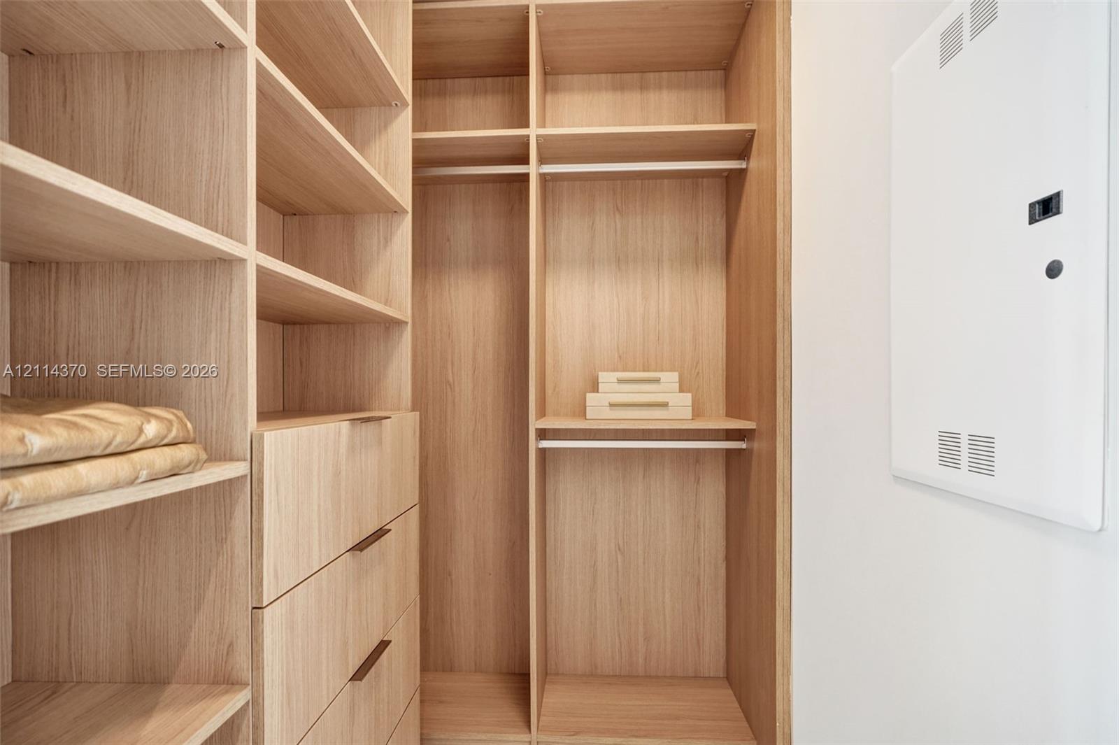 Built-in wood-finish cabinetry featuring open shelving, integrated hanging rods, and four pull-out drawers with slender hardware