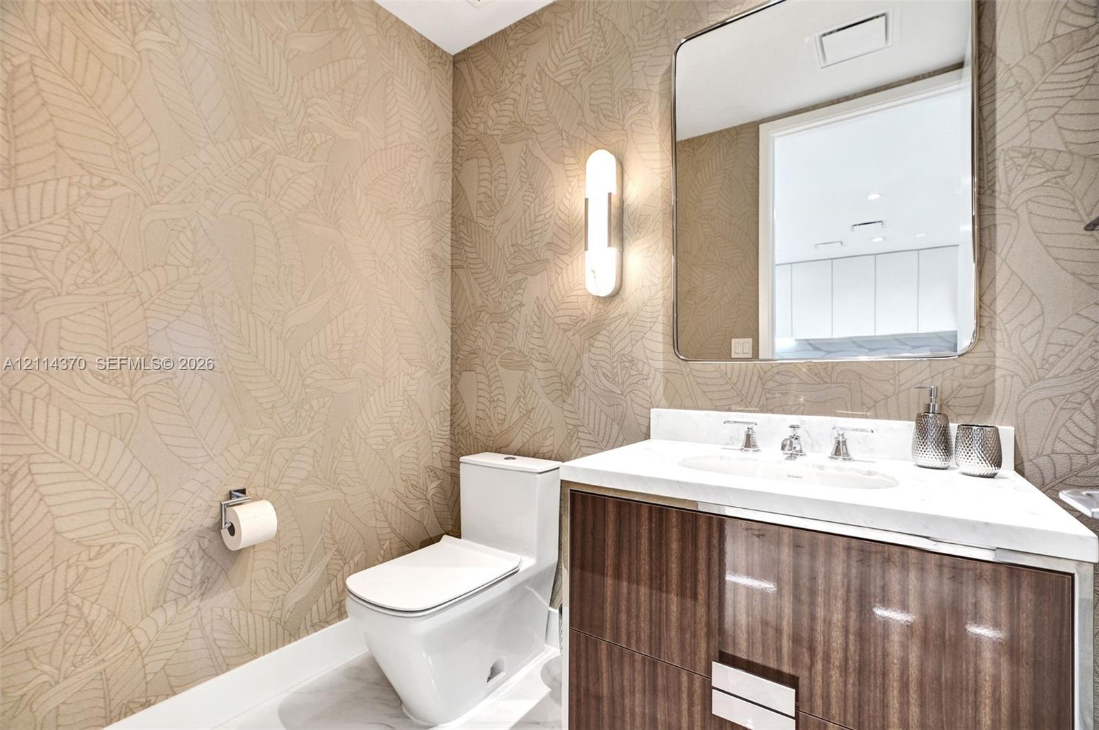 Wall-mounted vanity featuring wood-finish cabinetry, white countertop, integrated sink, vertical wall-mounted lighting, and patterned wallpaper