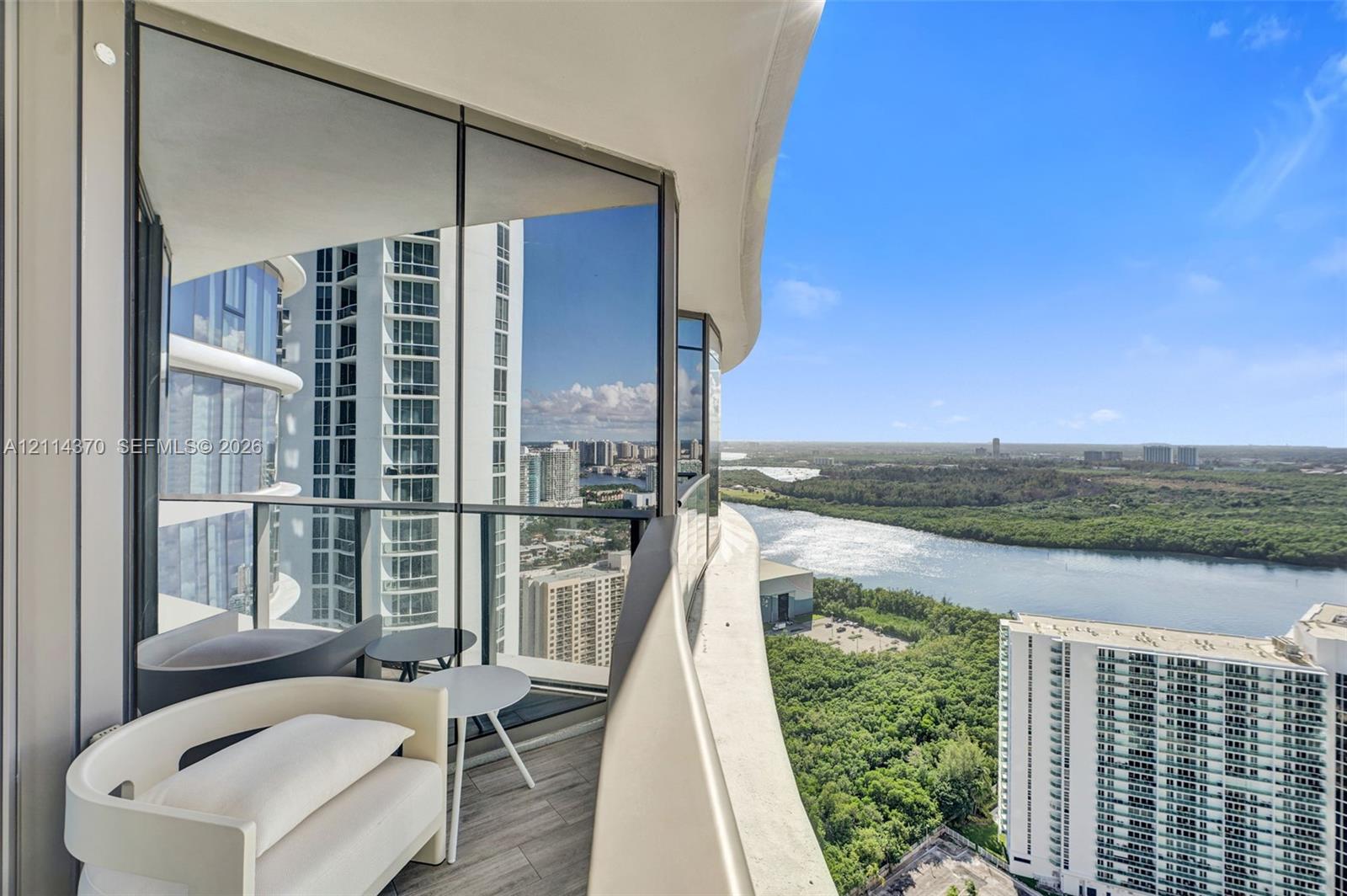 Curved exterior balcony featuring glass railing, wood-finish flooring, and expansive floor-to-ceiling glass paneling