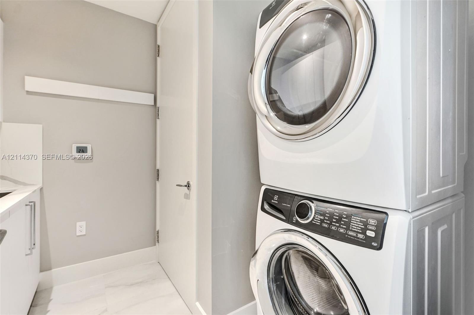 Laundry area featuring a stacked white front-load washer and dryer, stone-patterned tile flooring, integrated white cabinetry, and a solid-core interior door with modern metal hardware