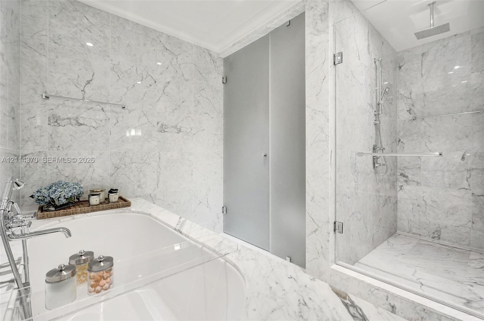 Floor-to-ceiling stone wall cladding, deep soaking tub with polished chrome deck-mounted faucet, and glass-enclosed walk-in shower featuring a rainfall showerhead and handheld wand