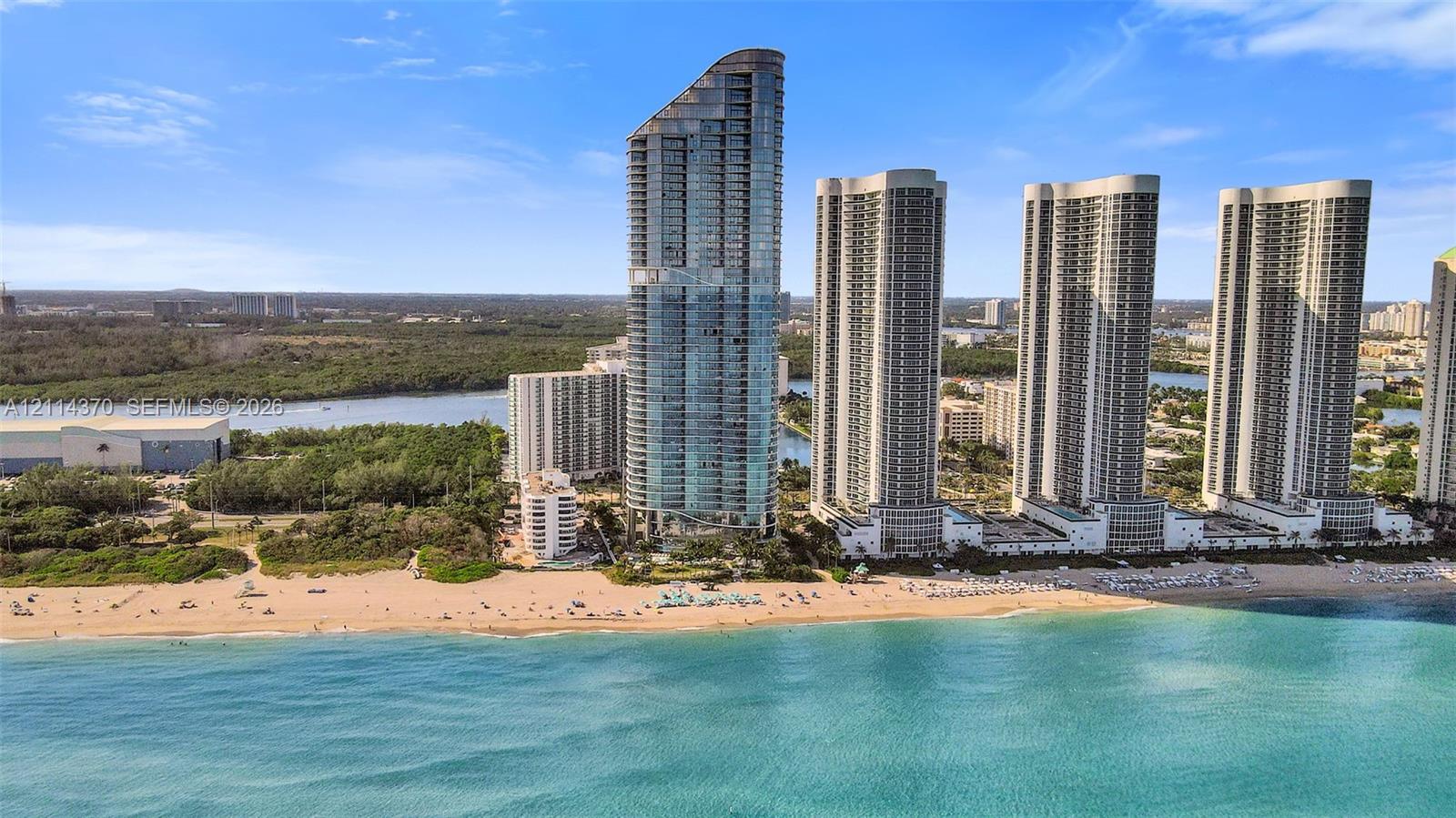 High-rise tower featuring glass-paneled exterior walls and direct oceanfront access to a sandy beach