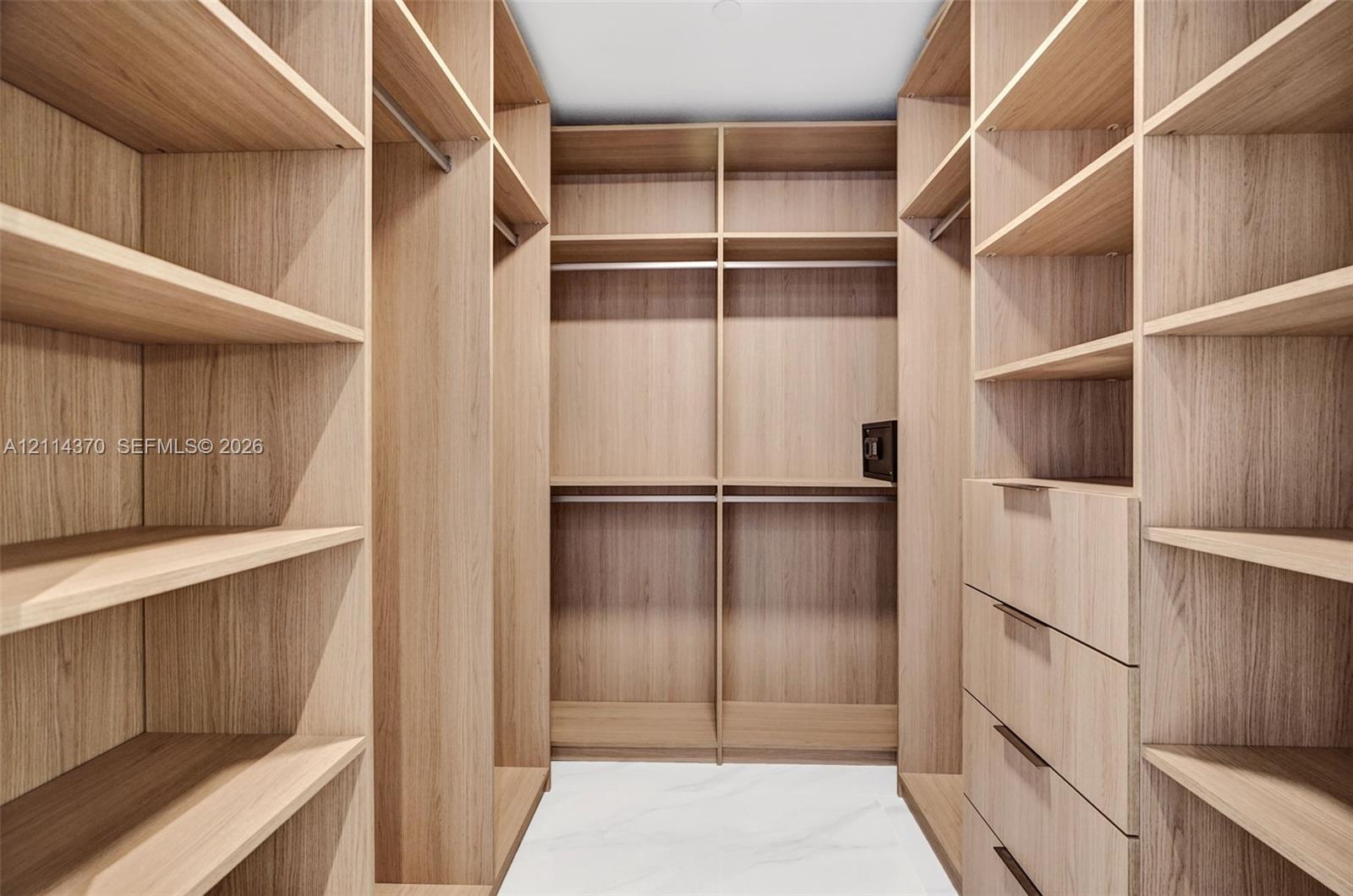 Custom walk-in closet featuring extensive wood-finish shelving, integrated clothing rods, a built-in safe, and a column of four drawers with matte hardware