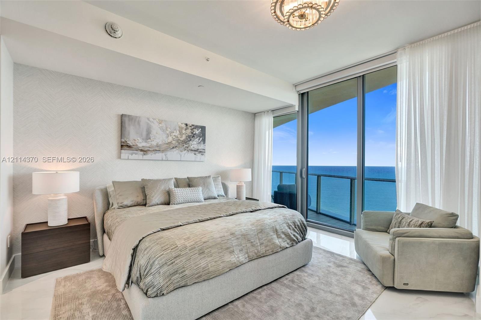 Floor-to-ceiling glass sliding doors, private balcony, polished stone flooring, textured wall covering, and a modern circular chandelier