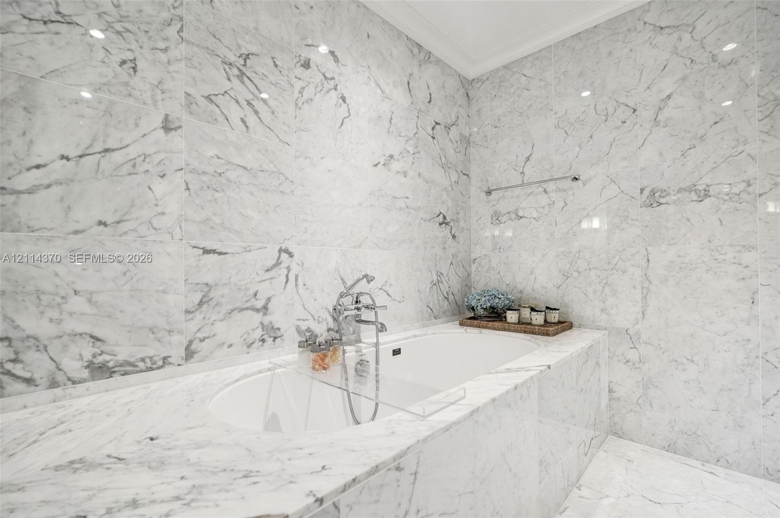 Soaking tub enveloped in floor-to-ceiling stone tile with matching surround and polished metal wall-mounted faucet