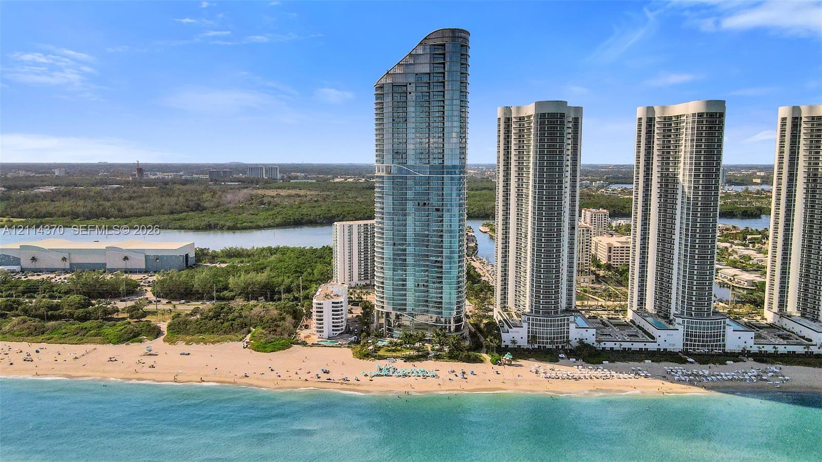 High-rise residential tower featuring floor-to-ceiling glass paneling, tiered architectural design, and direct beachfront positioning