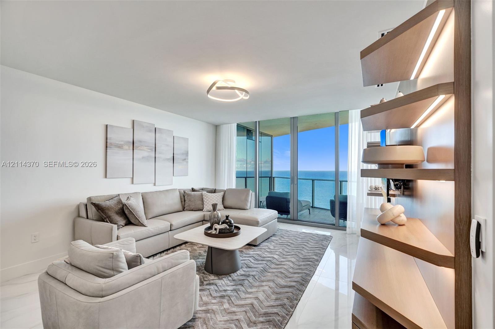 Floor-to-ceiling glass sliding doors with access to a balcony, built-in recessed wood-finish shelving with integrated LED lighting, and polished stone-finish flooring