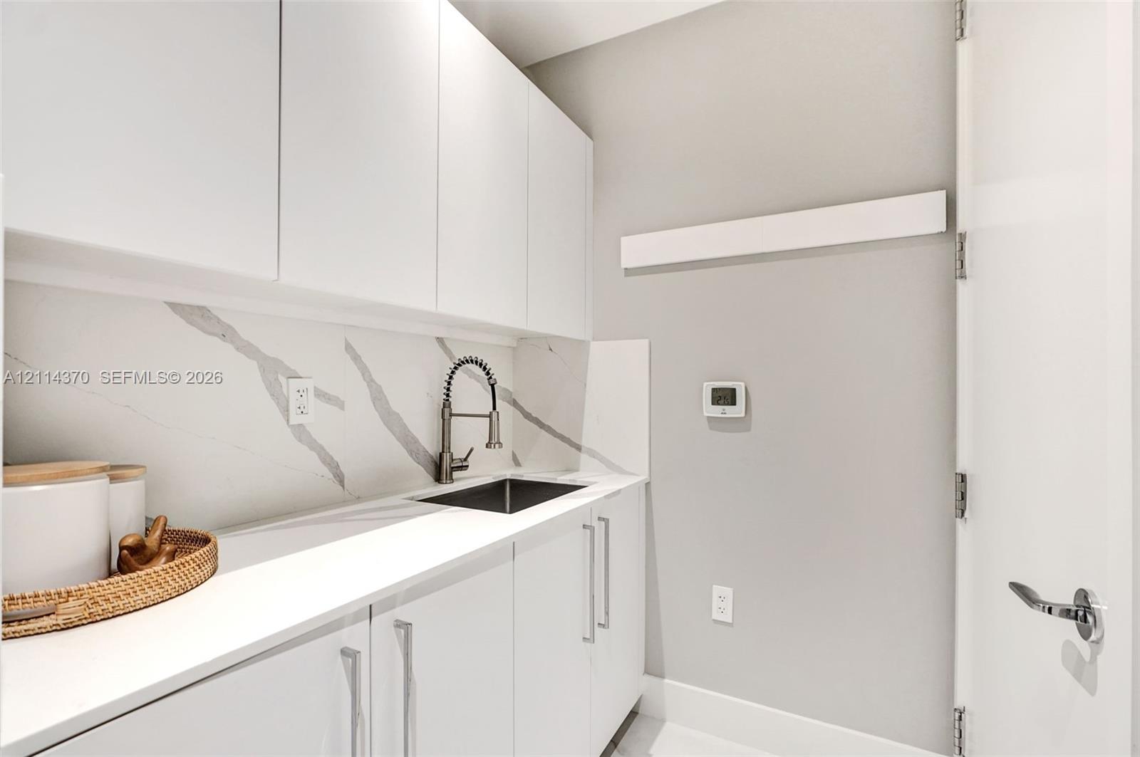Minimalist cabinetry with polished hardware, stone-patterned backsplash, undermount sink featuring a high-arc pull-down faucet, and solid-surface countertop