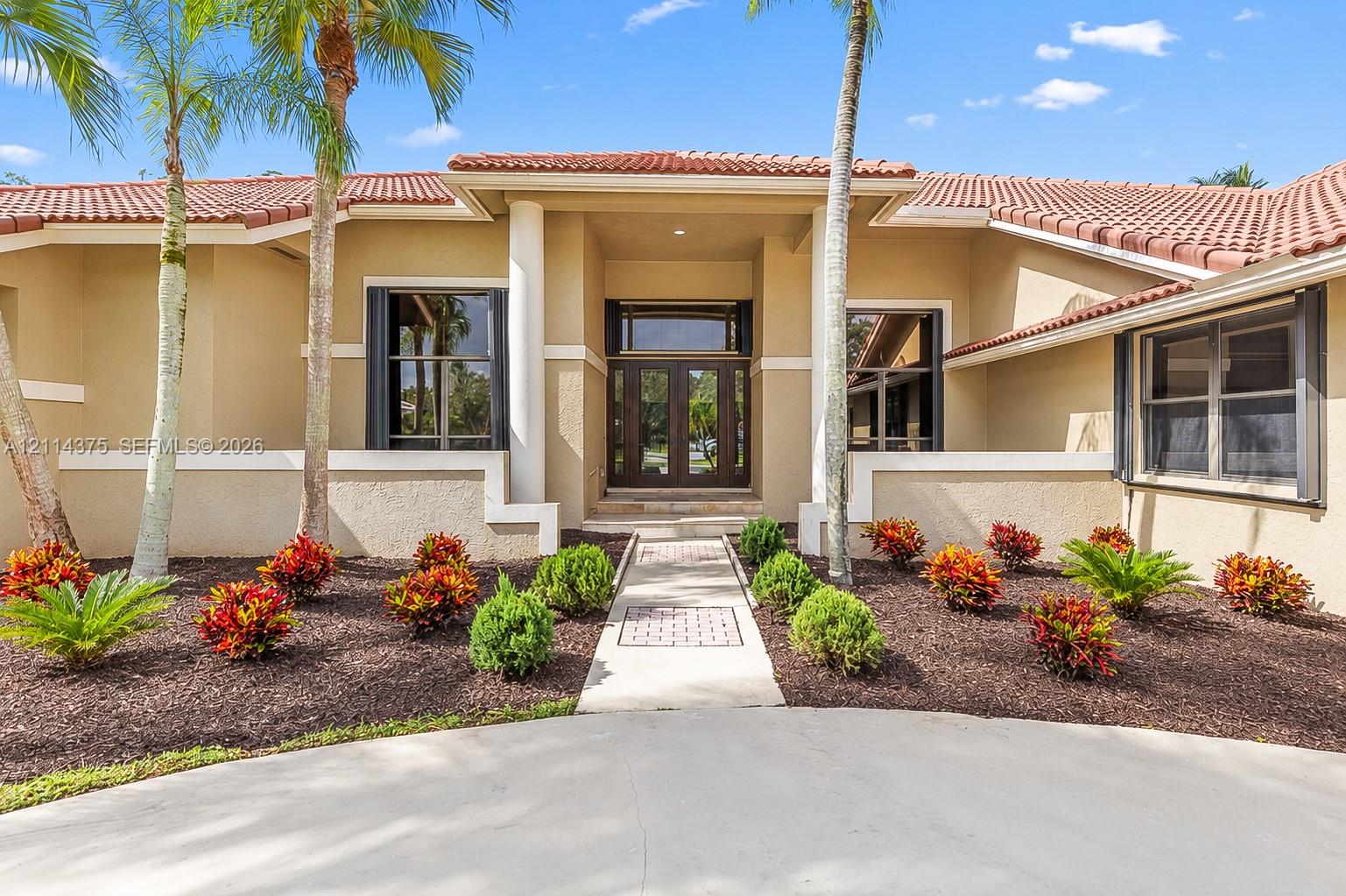 Stucco exterior featuring a terracotta tile roof, central recessed entryway with dual glass-paneled doors, decorative column accents, and a paved walkway