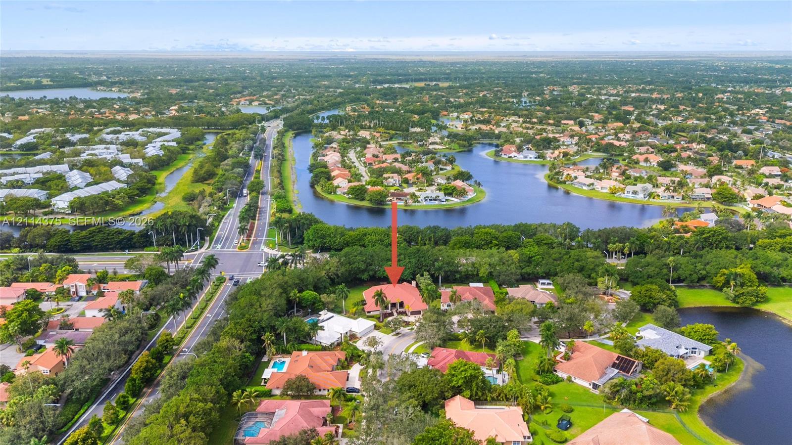 Aerial perspective of a multi-level residence featuring a clay tile roof, paved driveway, expansive lot with mature landscaping, and proximity to multiple water features