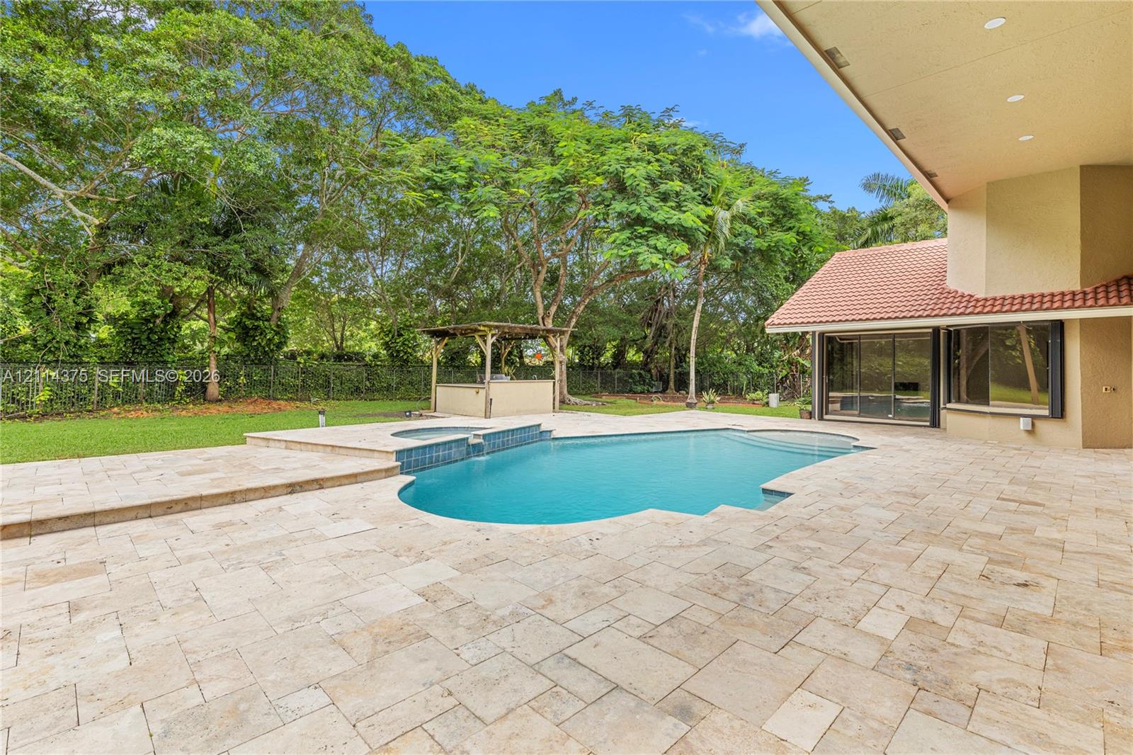 Extensive stone-paver patio featuring a swimming pool with an integrated spa, built-in outdoor kitchen structure, and manicured lawn