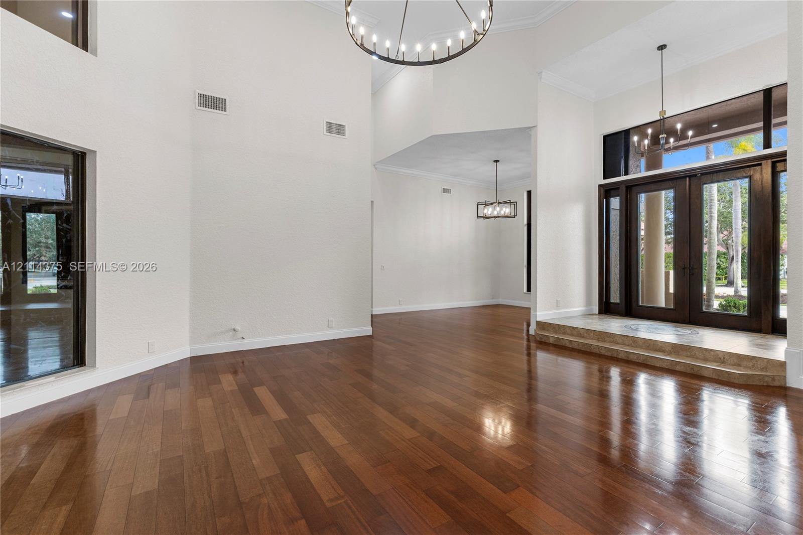 Grand foyer featuring high ceilings, wood-finish flooring, double-door entry, a circular chandelier, and a stone-tiled platform