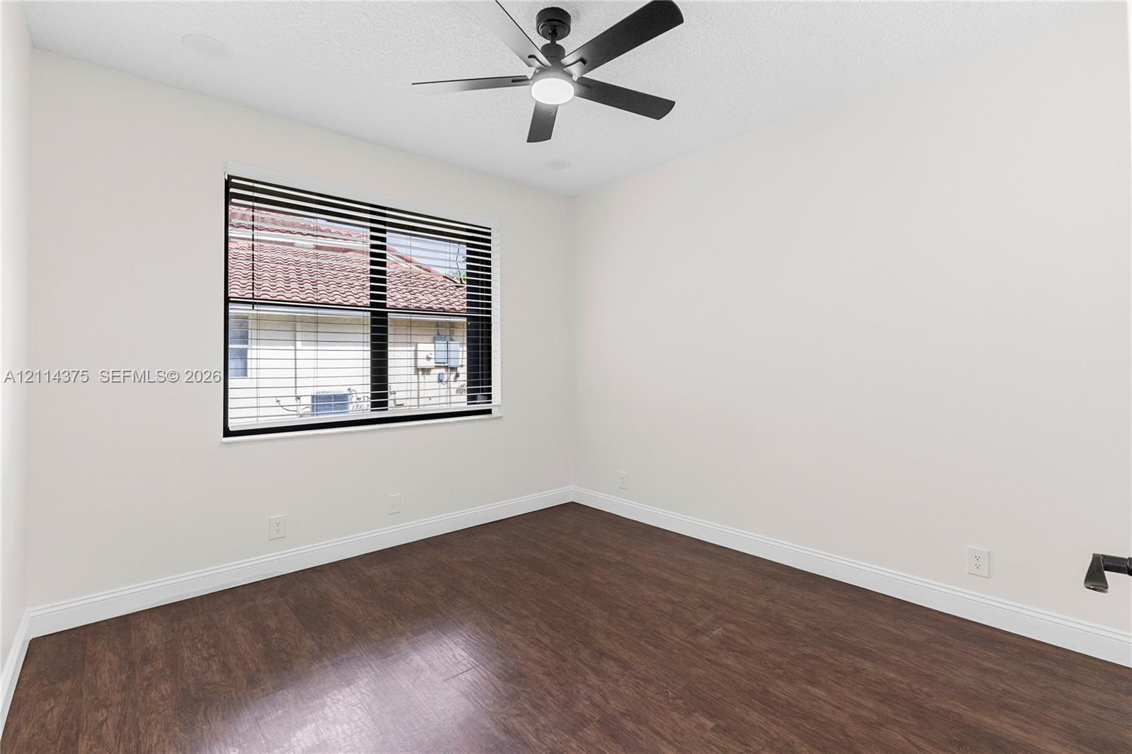 Interior room featuring dark-tone wood-finish flooring, a contemporary matte black ceiling fan with an integrated light, and a single window with horizontal blinds