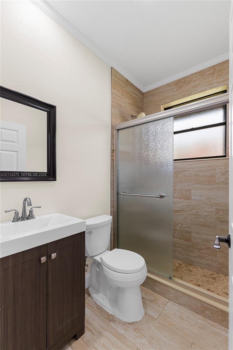 Bathroom featuring a dark wood-finish vanity, integrated rectangular sink, brushed chrome fixtures, stone-style tiled shower enclosure with sliding glass door, and neutral tile flooring