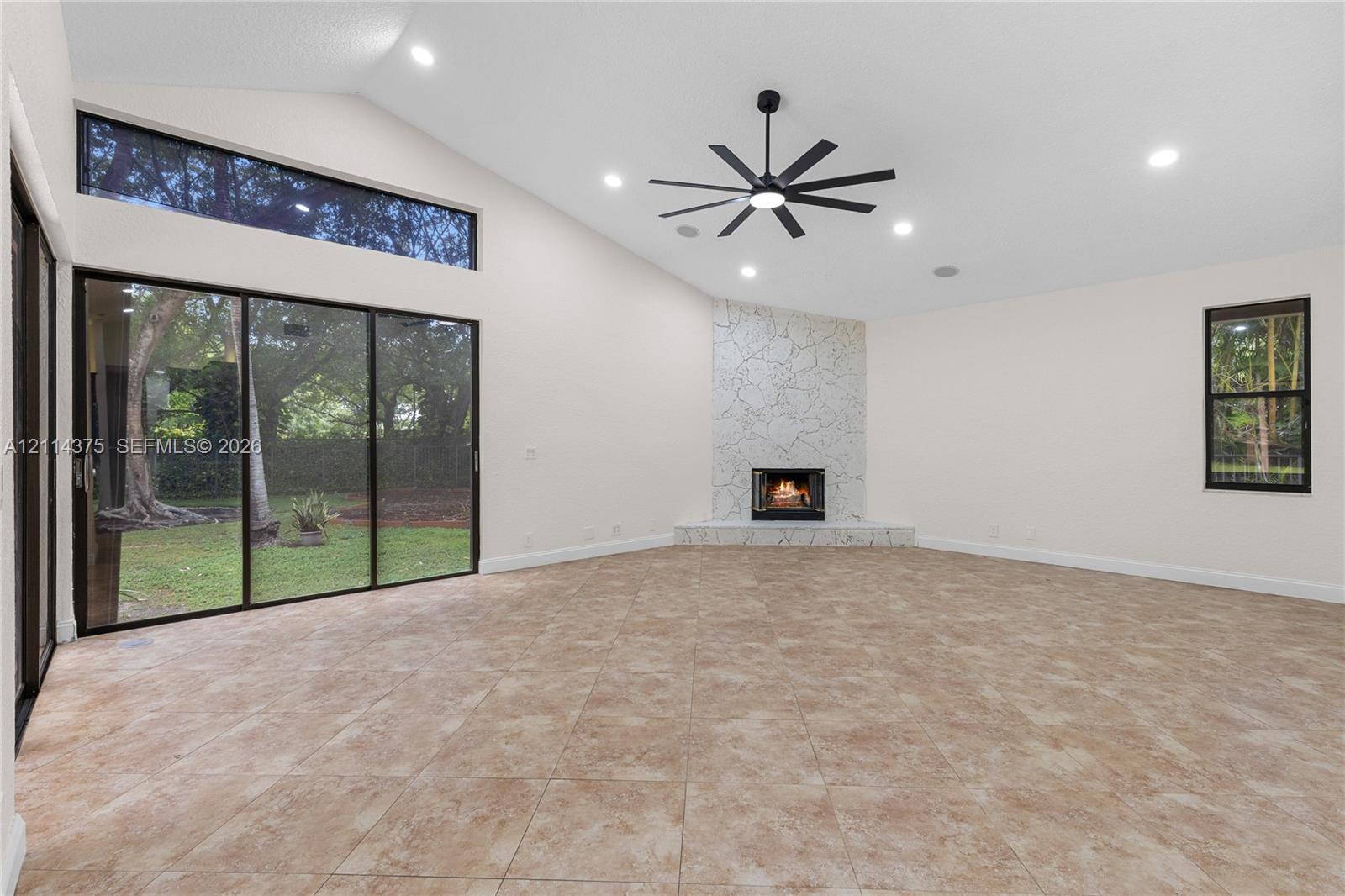Vaulted ceilings featuring recessed lighting, expansive glass sliding doors, floor-to-ceiling stone-faced fireplace with a raised hearth, and neutral tile flooring