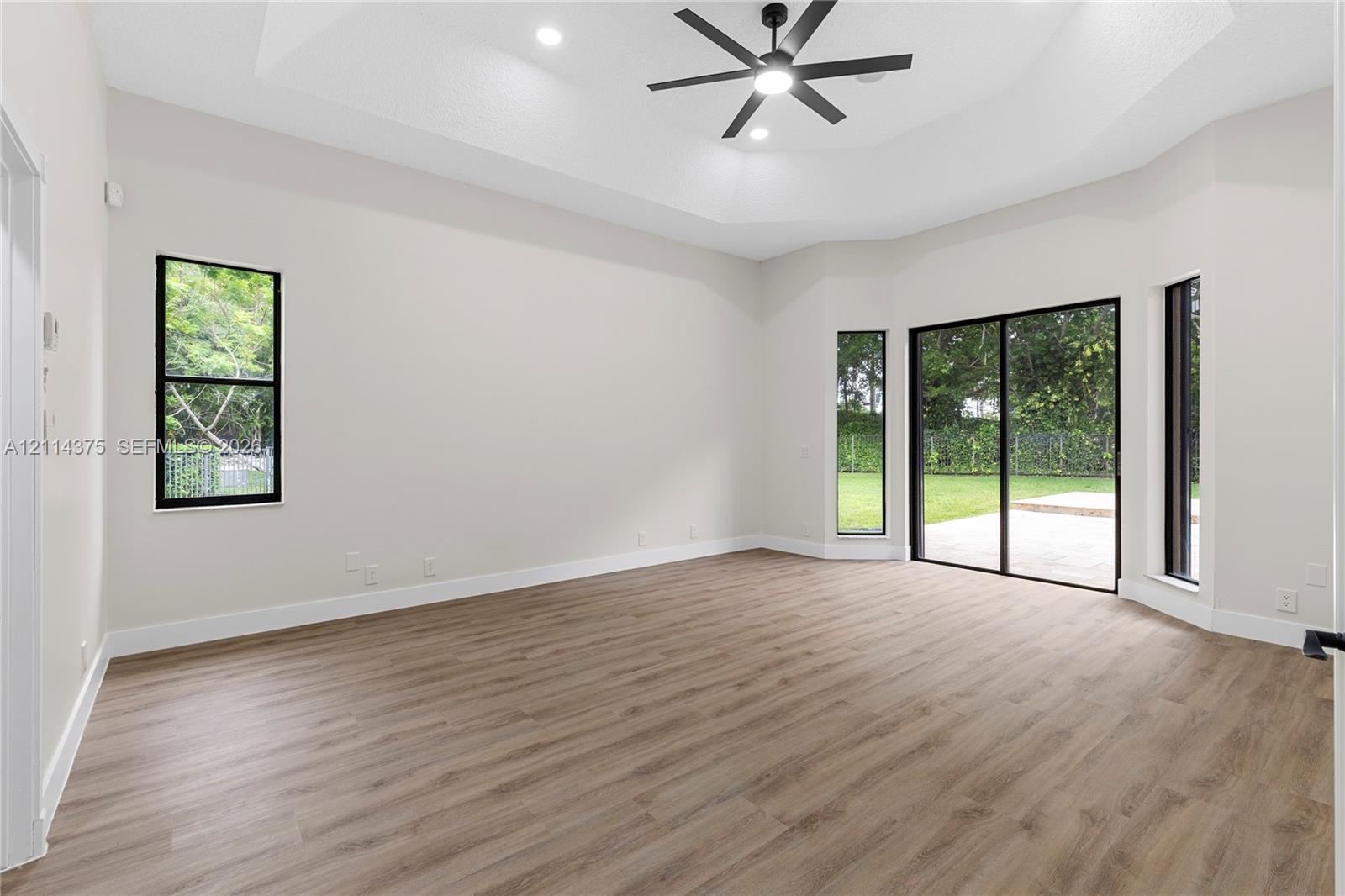 Tray ceiling with integrated recessed lighting, wood-finish flooring, black-framed windows, and sliding glass doors with exterior access