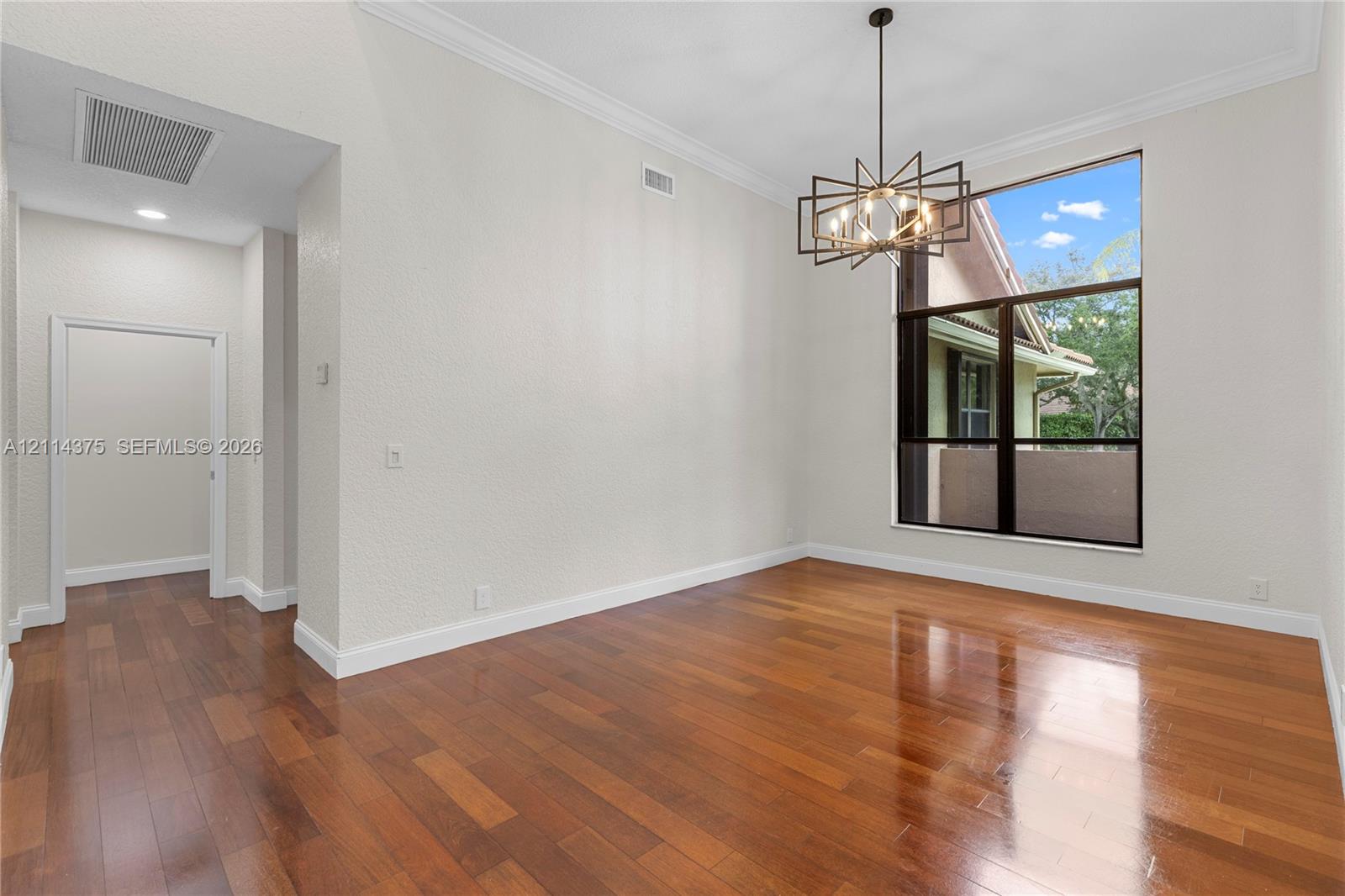 High-ceiling room featuring wood-finish flooring, a contemporary multi-arm metal chandelier, crown molding, and a large multi-pane window