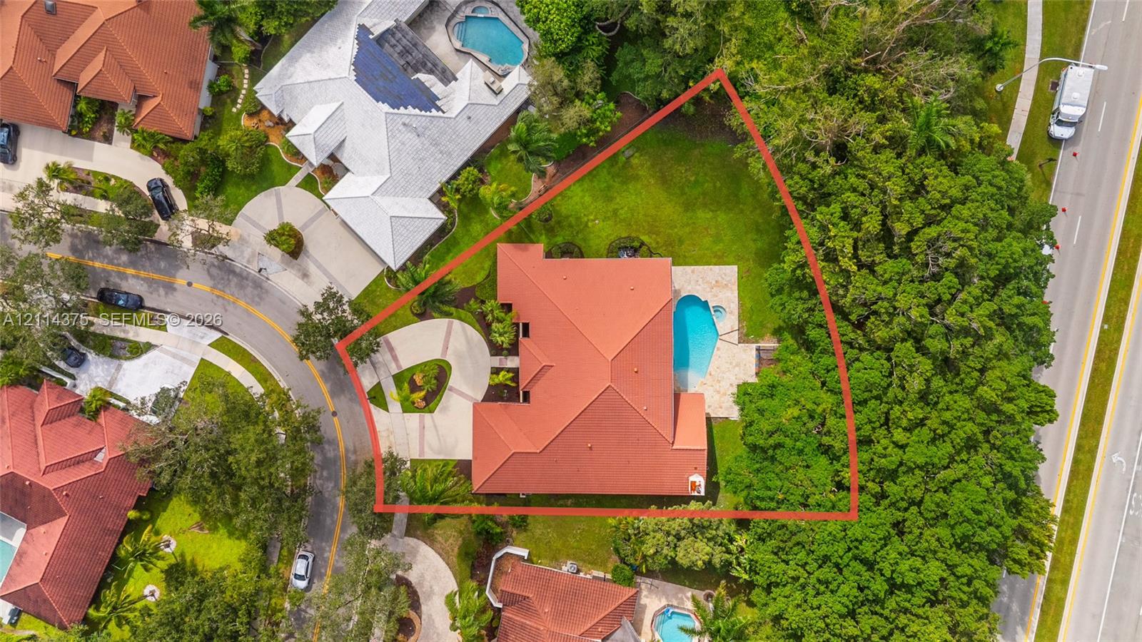 Aerial perspective of a property featuring a tile roof, a paved circular driveway, a rear swimming pool, and mature landscaping