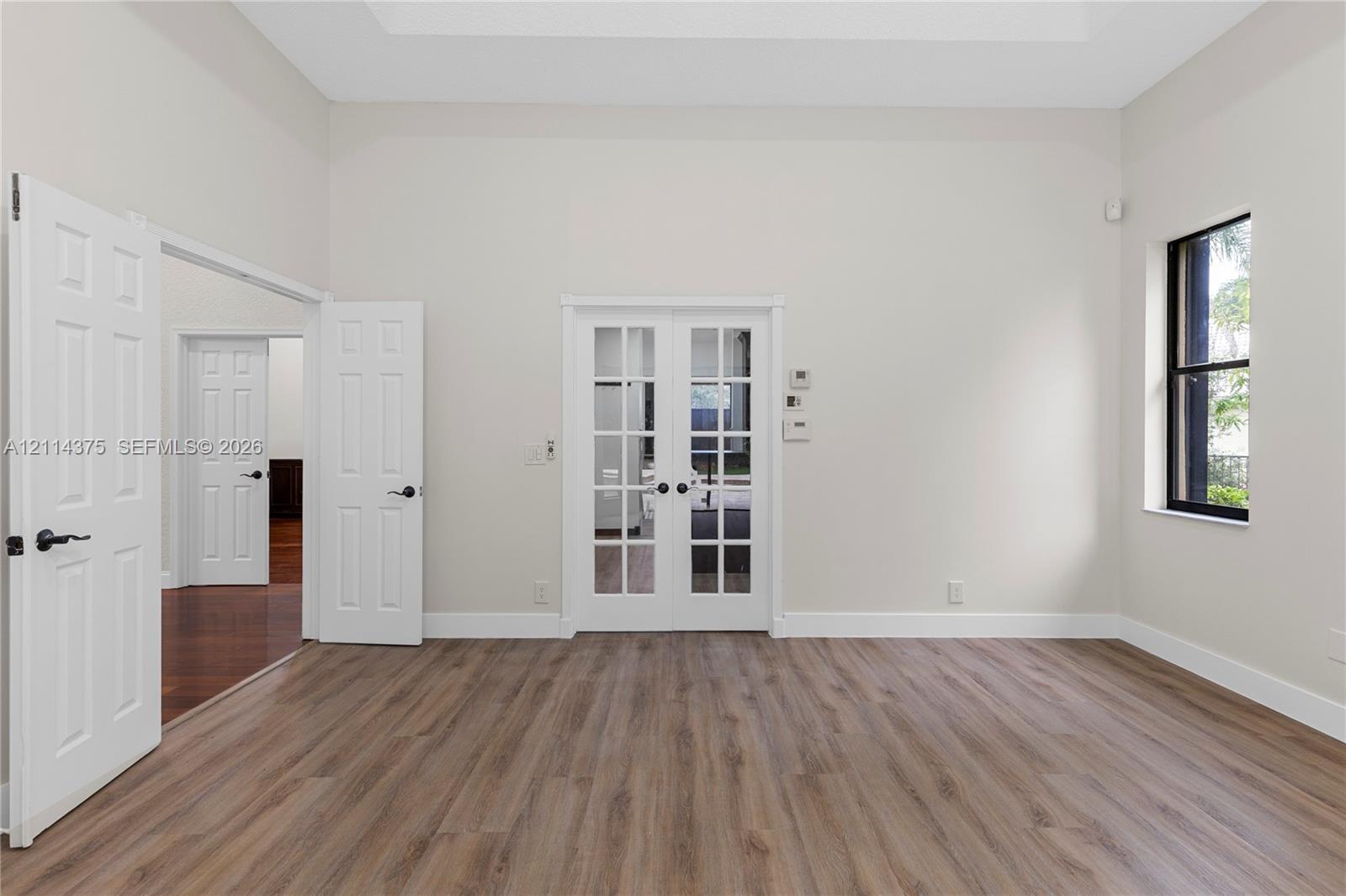 Room featuring high ceilings, wood-finish flooring, glass-paneled French doors, and a multi-pane window