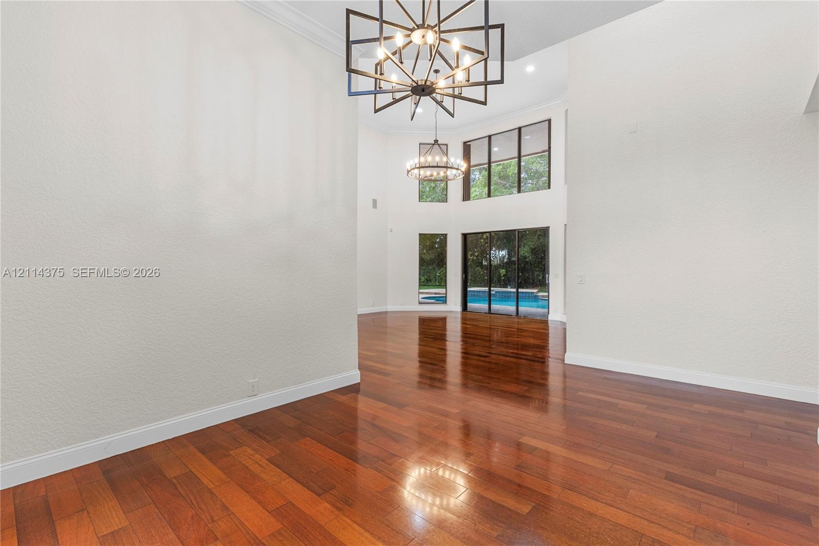 Two-story interior space featuring wood-finish flooring, high ceilings, geometric metal chandeliers, and oversized windows