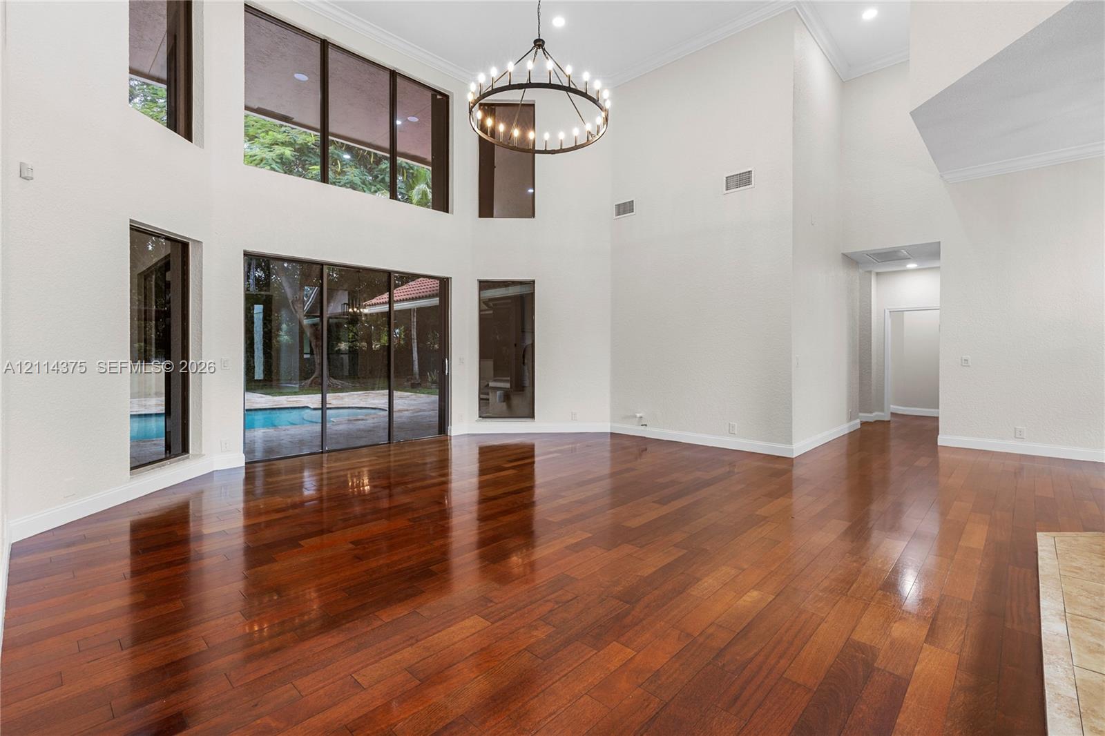 Double-height ceilings featuring floor-to-ceiling windows, wood-finish flooring, a large circular iron chandelier, and recessed lighting