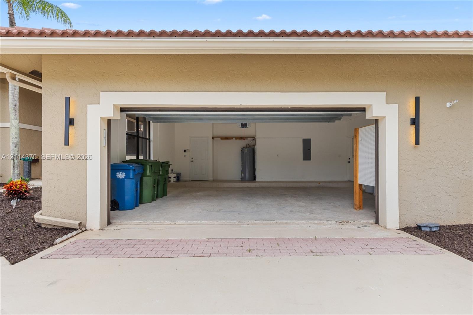 Stucco exterior garage featuring decorative trim, integrated wall-mounted lighting, and a concrete driveway with a paver accent strip