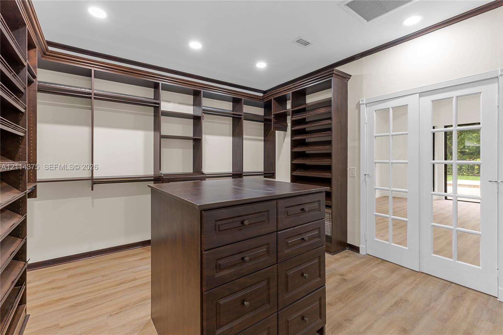 Custom storage cabinetry featuring extensive shelving, a central island with integrated drawers, wood-finish flooring, recessed lighting, and white French doors