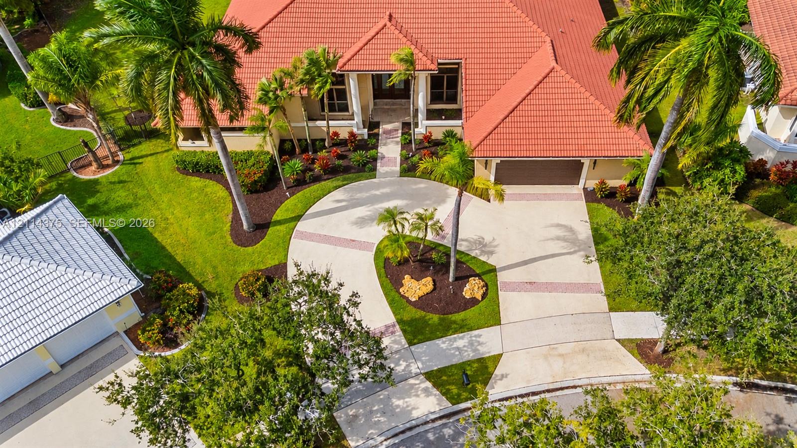 Exterior featuring a tile roof, circular driveway, multi-car garage, manicured landscaping, and mature palm trees