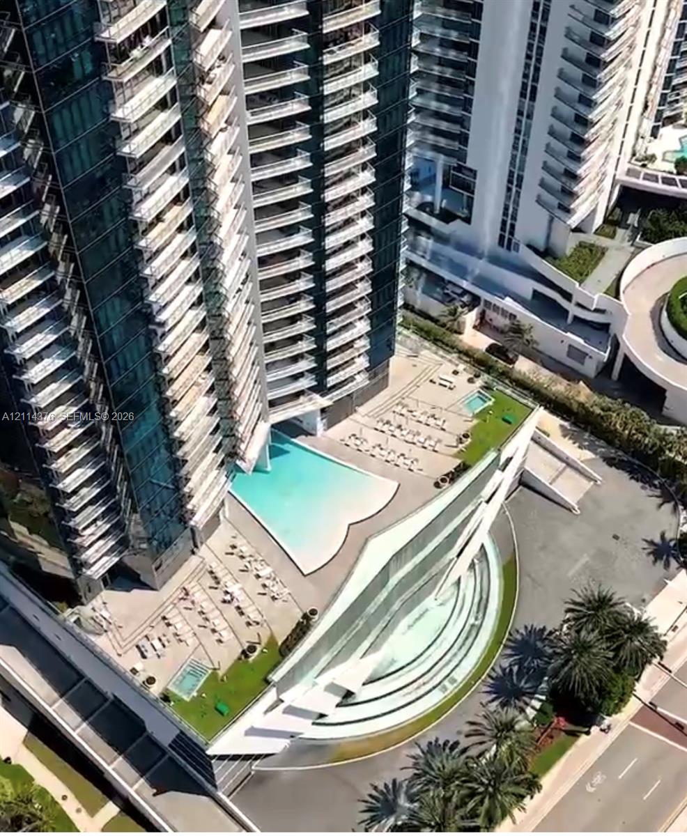 High-rise architectural exterior featuring tiered glass balconies, an expansive multilevel swimming pool area, multi-level terrace decks, and landscaped ground-level hardscaping