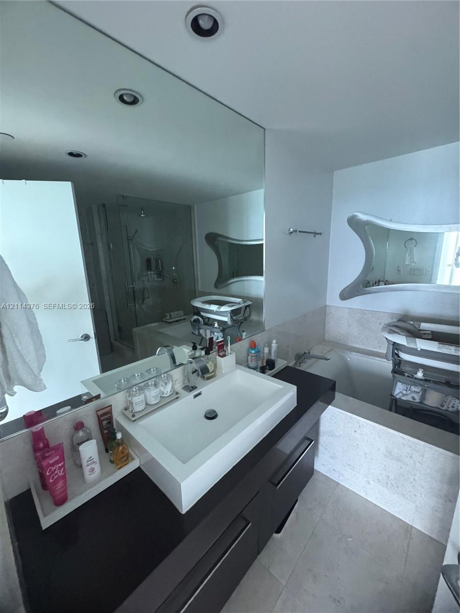 Contemporary bathroom featuring a dark-finish floating vanity, rectangular vessel sink, stone-surround soaking tub, and recessed ceiling lighting