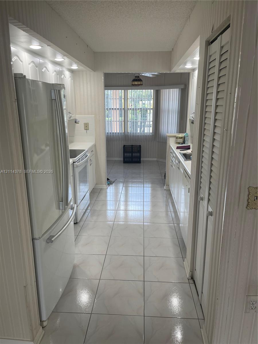 Galley-style kitchen featuring tile flooring, white cabinetry, integrated recessed lighting, and white appliances