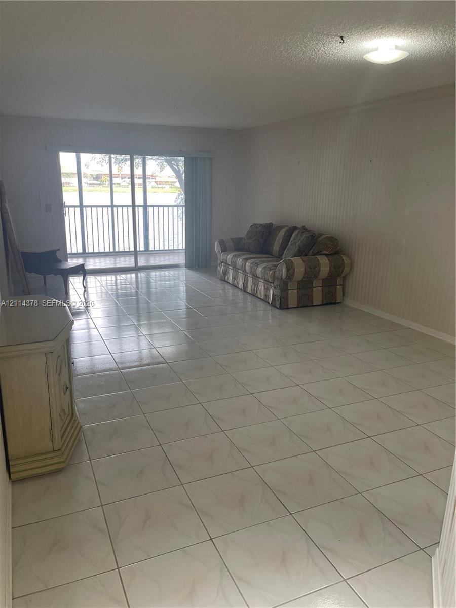 Large living area featuring neutral tile flooring, vertical wall paneling, and sliding glass doors with access to a railed balcony