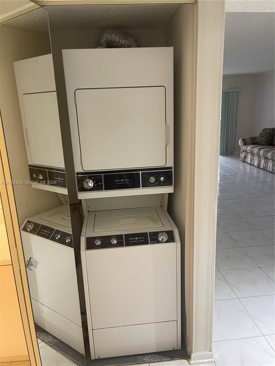 Stacked white laundry appliance unit housed within a closet featuring mirrored bi-fold doors