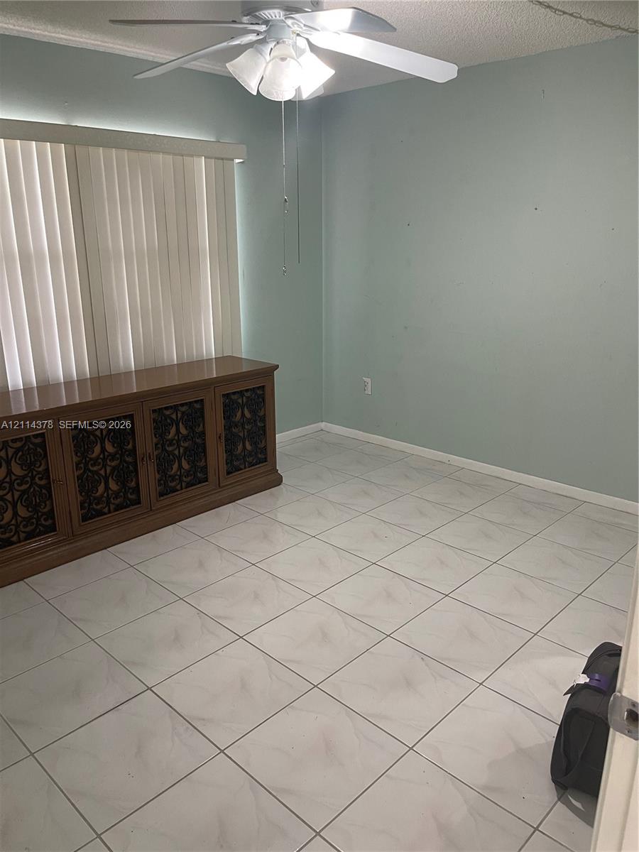Room featuring large-format tile flooring, a multi-blade ceiling fan with integrated light fixture, and horizontal window blinds